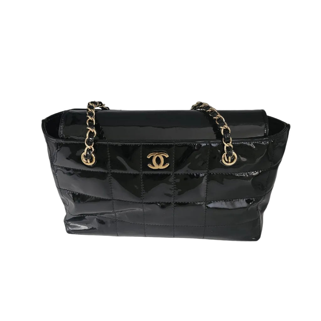 A black quilted patent leather handbag with gold-tone chain straps and a gold interlocking CC logo on the front, photographed against a light gray studio backdrop.