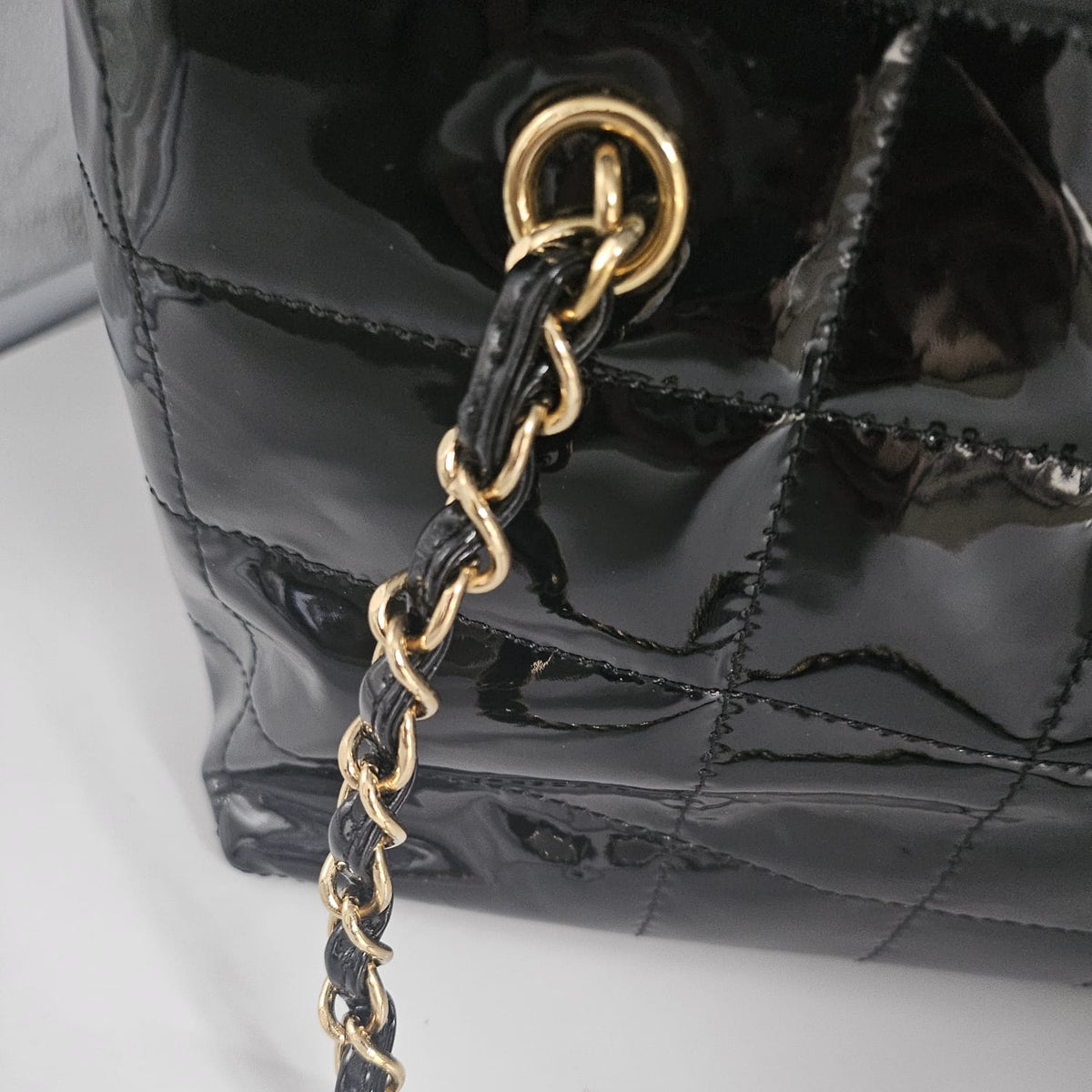 Close-up of a glossy black quilted handbag with a black-and-gold chain strap and gold-tone hardware on a light surface.