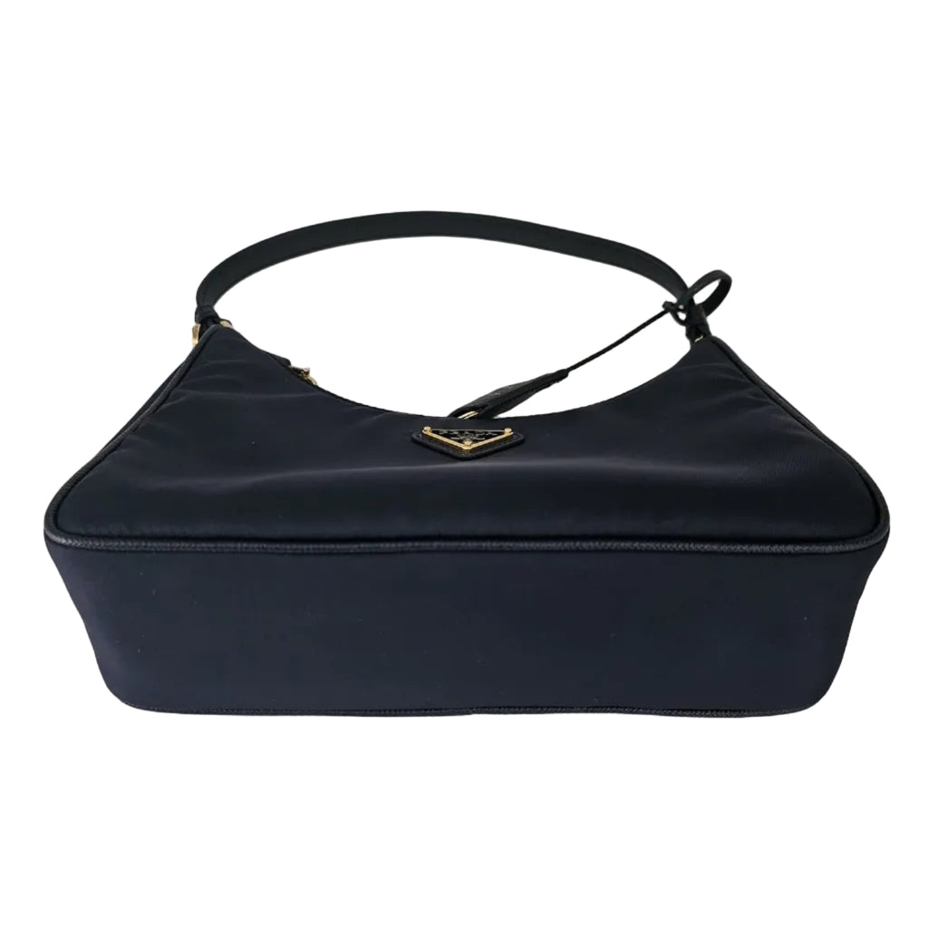 A navy blue nylon shoulder bag with a gold-tone metal logo clasp, photographed on a neutral light gray background.