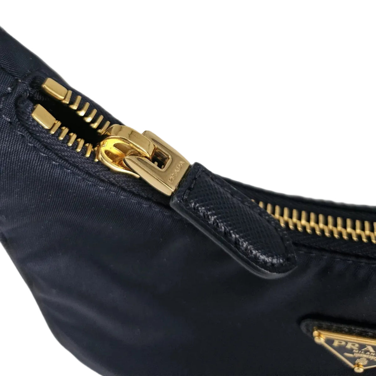 Close-up of a navy blue Prada nylon bag with gold-tone hardware, showing a zipper pull and a small triangular Prada logo plaque.