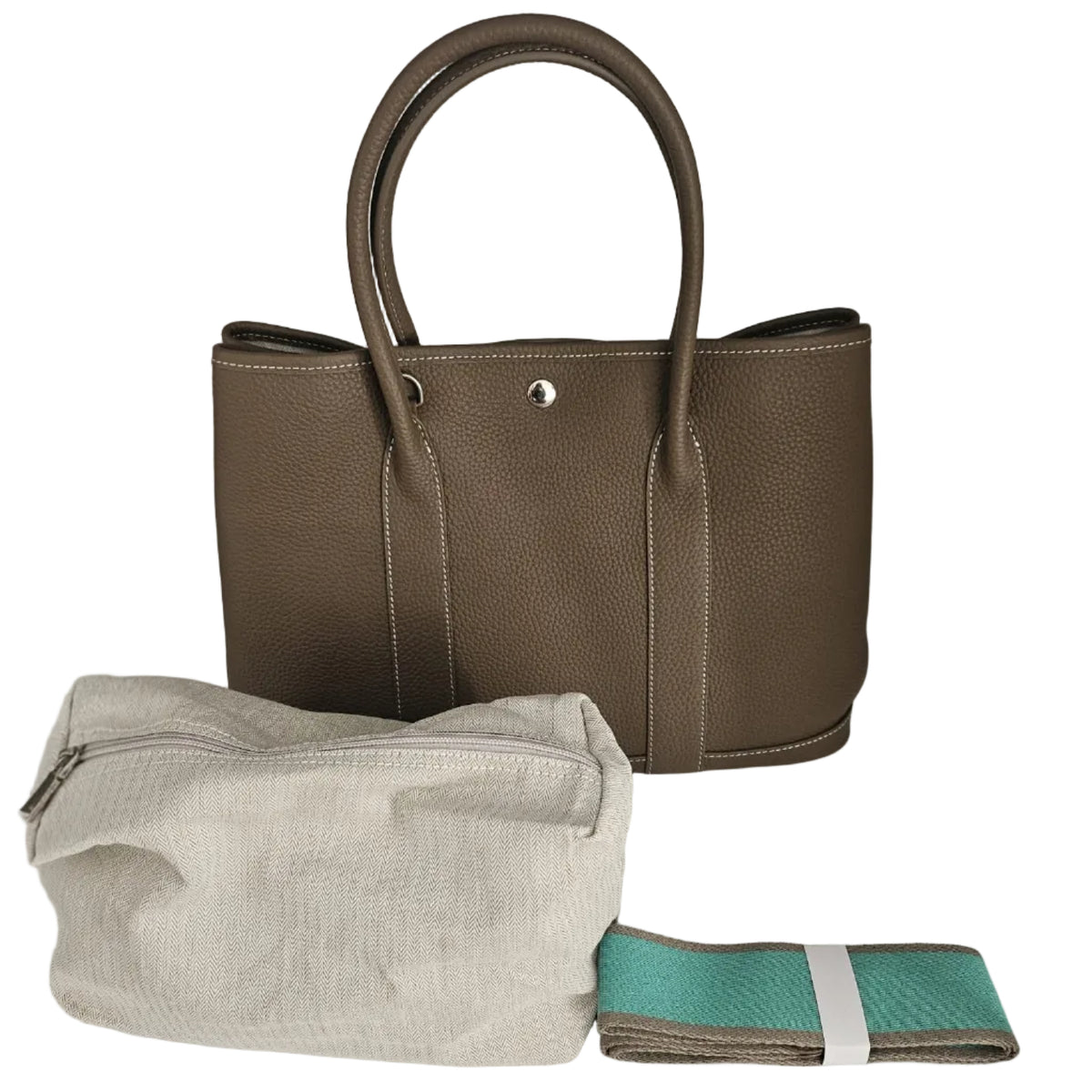 A taupe brown pebbled leather tote bag displayed with a light beige canvas dust bag and a folded teal and brown accessory wrapped in a white band, set against a plain light gray background.